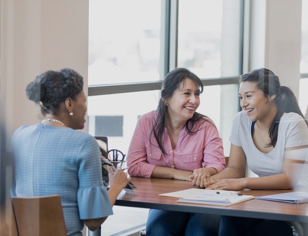 Mother and daughter sit at desk talking to female financial advisor