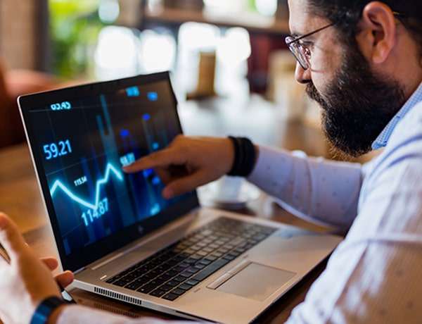 Man with beard and glasses points to chart on computer screen