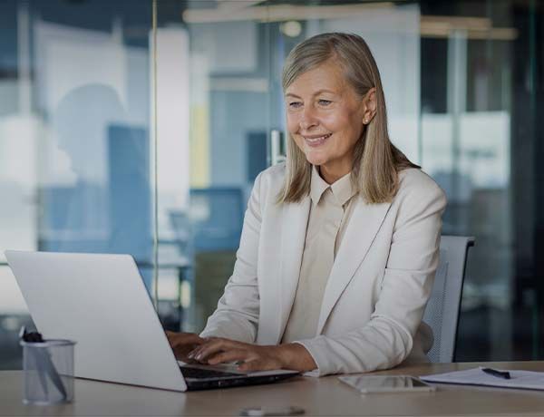 Retirement age woman sits at desk working on laptop